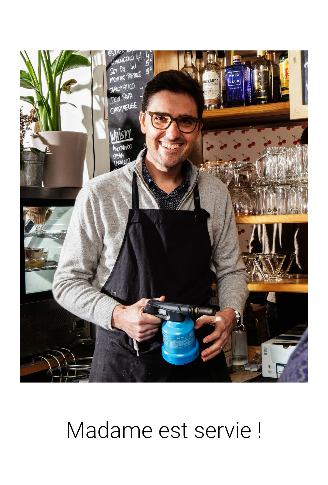 a man in a black apron and glasses holding a blue mug